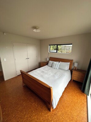 Une chambre à coucher avec un lit en bois, du linge de lit blanc, une table de chevet avec une lampe, une armoire et une fenêtre donnant sur un beau paysage.