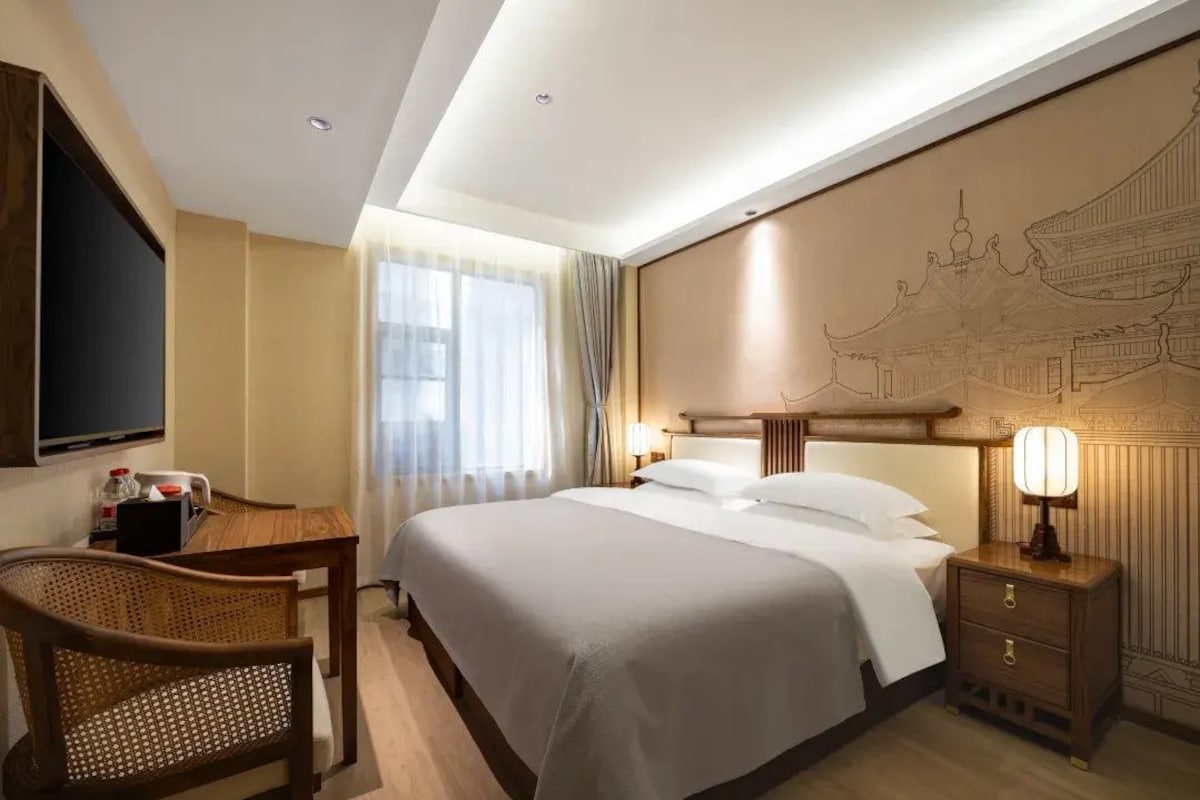 Une chambre d’hôtel comprenant un lit, une table de chevet, une lampe, une chaise et un mur orné d’un motif décoratif.