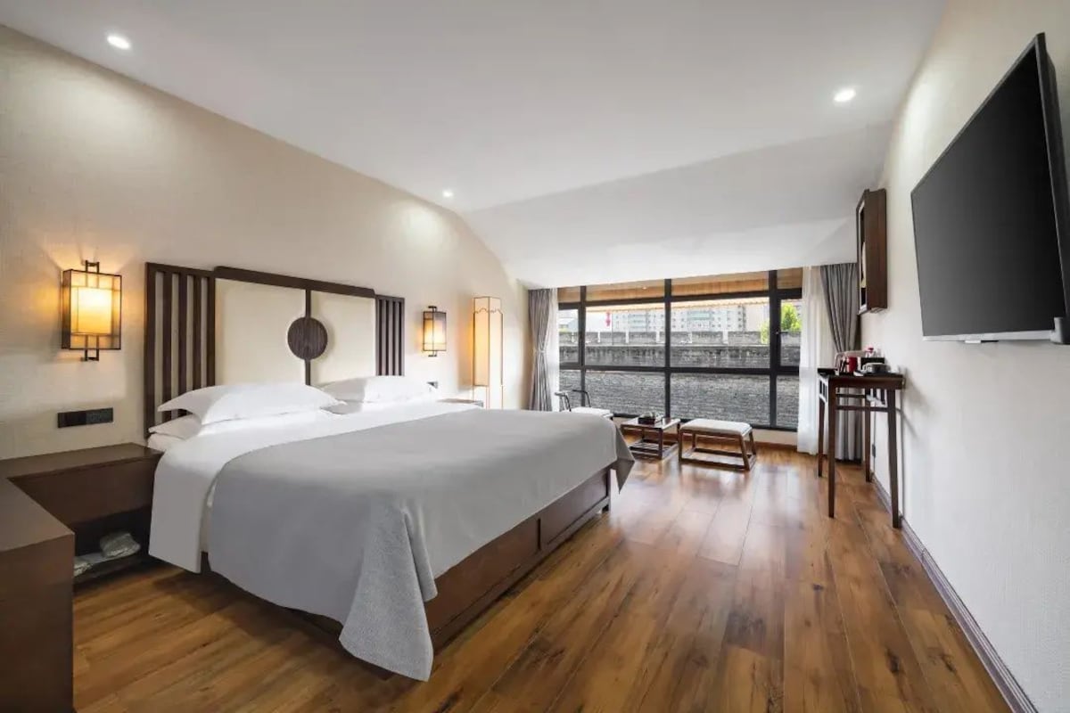Une chambre d’hôtel moderne dotée d’un grand lit, de tables de chevet, d’un téléviseur à écran plat et d’une fenêtre offrant une vue agréable.