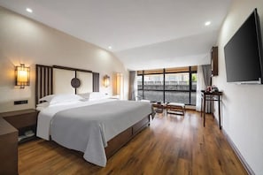 Une chambre d’hôtel moderne dotée d’un grand lit, de tables de chevet, d’un téléviseur à écran plat et d’une fenêtre offrant une vue agréable.