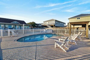 A swimming pool with lounge chairs and a wooden deck, surrounded by a wooden fence. - Few Blocks to Beach • Pool Access + Golf Cart Zone | Beach Therapy (Port Aransas)