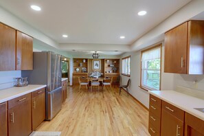 A kitchen with wooden cabinets, a refrigerator, a dining table with chairs, and a window with a view.