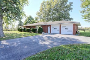 A two-story brick building with a garage, surrounded by trees and a gravel driveway.