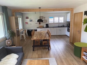 A modern kitchen with white cabinets, a wooden dining table, and a green accent chair. - New Listing (Schattenhalb)