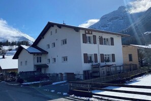 A two-story building with a sloped roof, a fenced driveway, and a mountain backdrop. - New Listing (Schattenhalb)