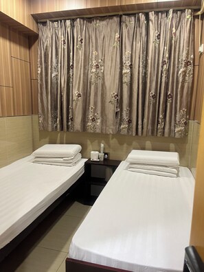 A hotel room with two single beds, a small table with a cup and tissues, and a curtain with floral patterns. - ME EASY HOSTEL (MongKok)
