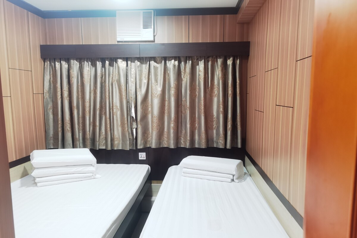 A room with two single beds, a window with curtains, and a wall-mounted air conditioner.