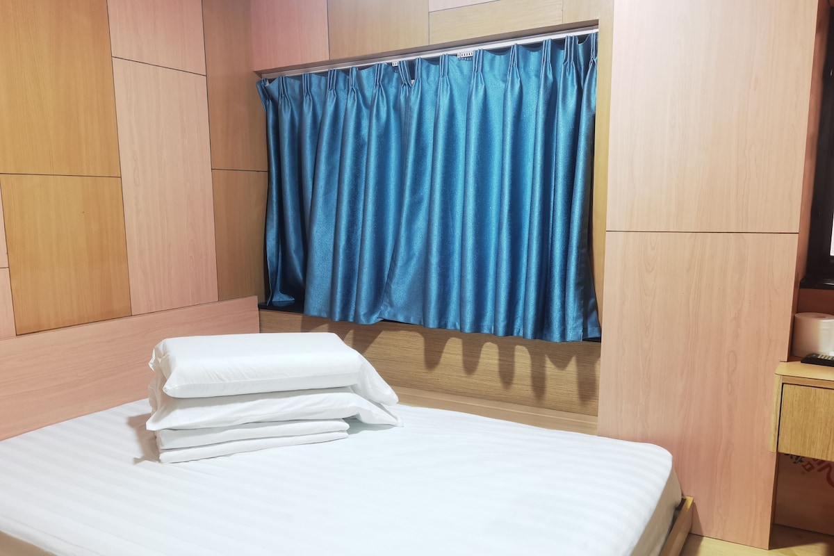 A hotel room with a bed, a blue curtain, and a wooden wardrobe.