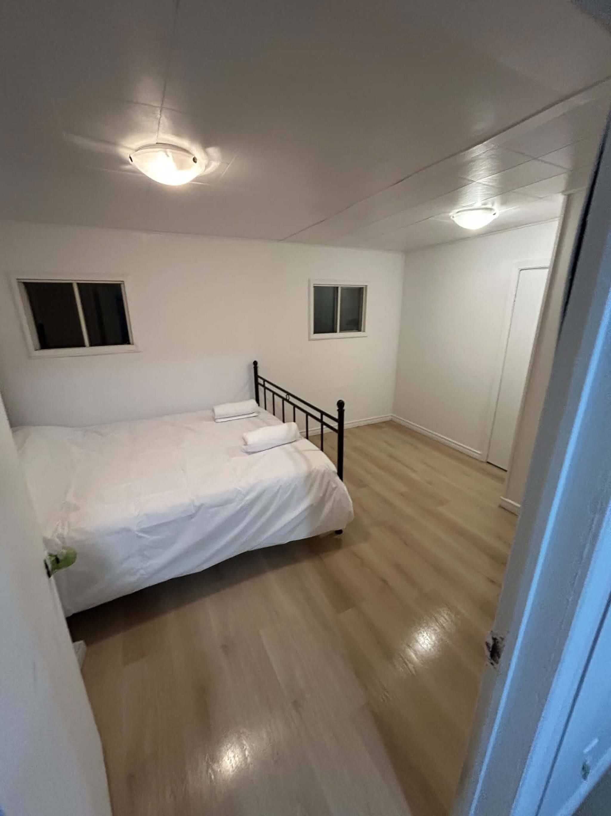 A bedroom with a bed, two windows, a door, and a light fixture.