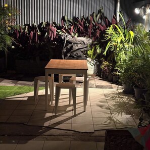An outdoor patio area with a wooden table and chairs, surrounded by various potted plants. - Spacious, Stylish & Quite Greenslopes Apartment close to Hospitals & the City (Greenslopes)
