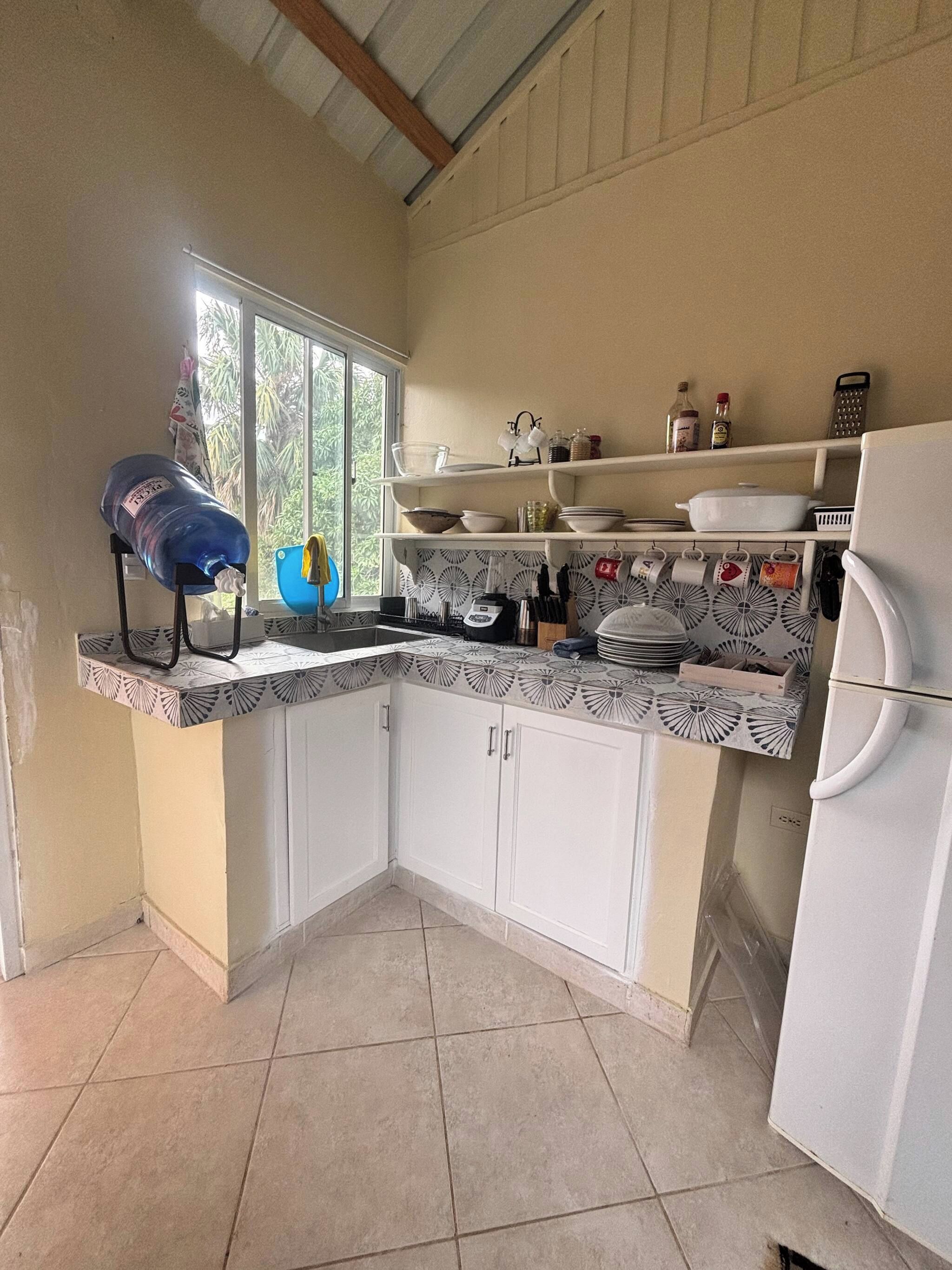A compact kitchen with white cabinets, a white refrigerator, and a window providing natural light.