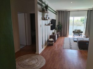 Een woonkamer met een flatscreen televisie, een bank, een bijzettafeltje en een uitzicht op de omgeving door grote ramen.