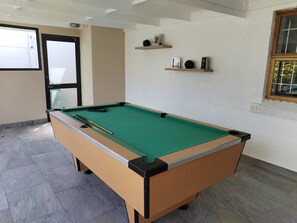 Een pooltafel in een ruimte met witte baksteenmuren, een raam en een deur.