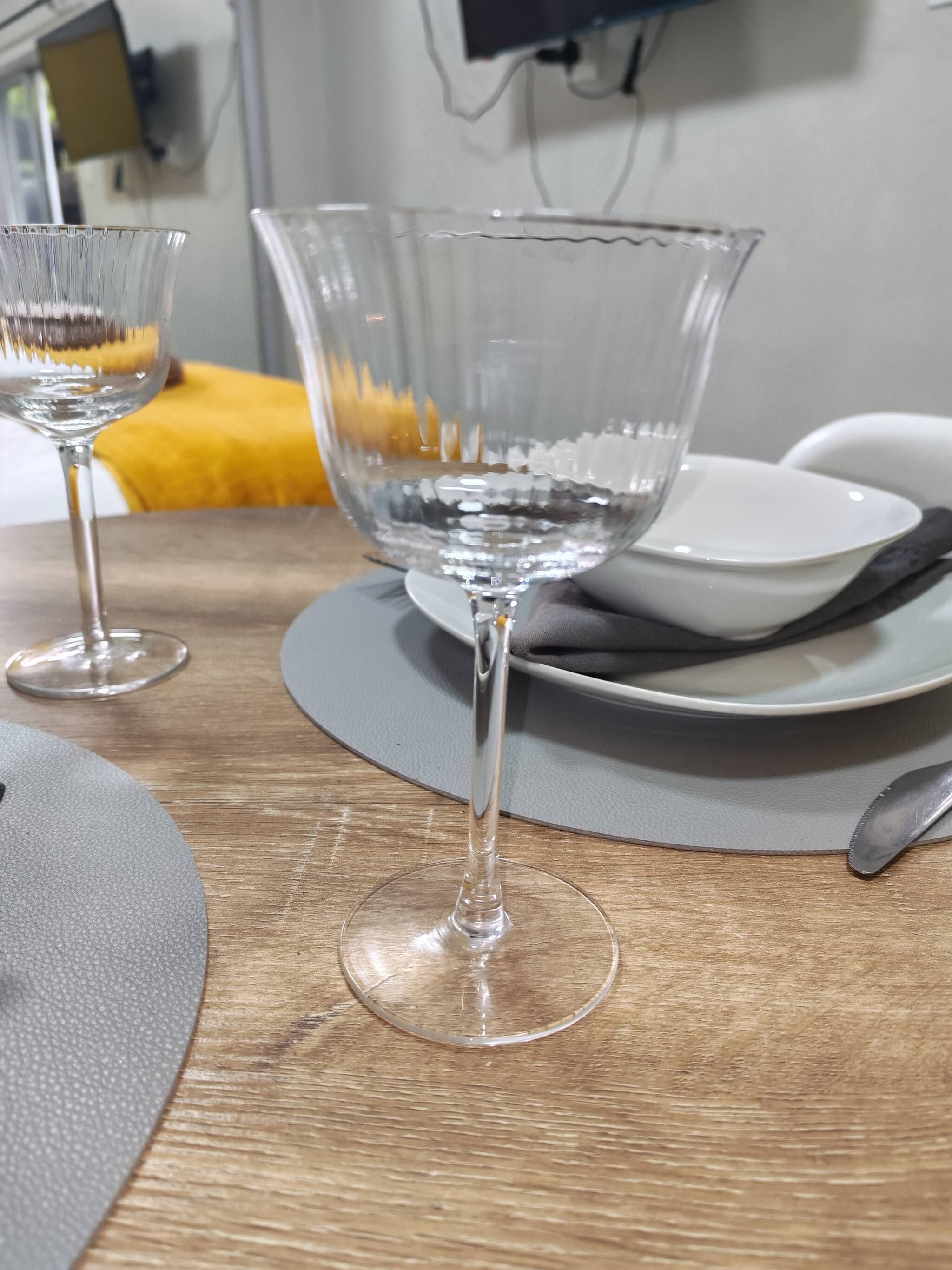 A table with two clear glass wine glasses, a white plate, and a gray placemat.