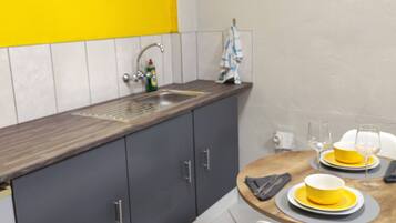A kitchen with a yellow backsplash, grey cabinets, and a round dining table with yellow plates and glasses.