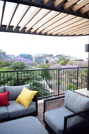 A balcony with a view of a cityscape and purple flowering trees. - Saxon Square Voyage Work, Rest & Recharge (Johannesburg)