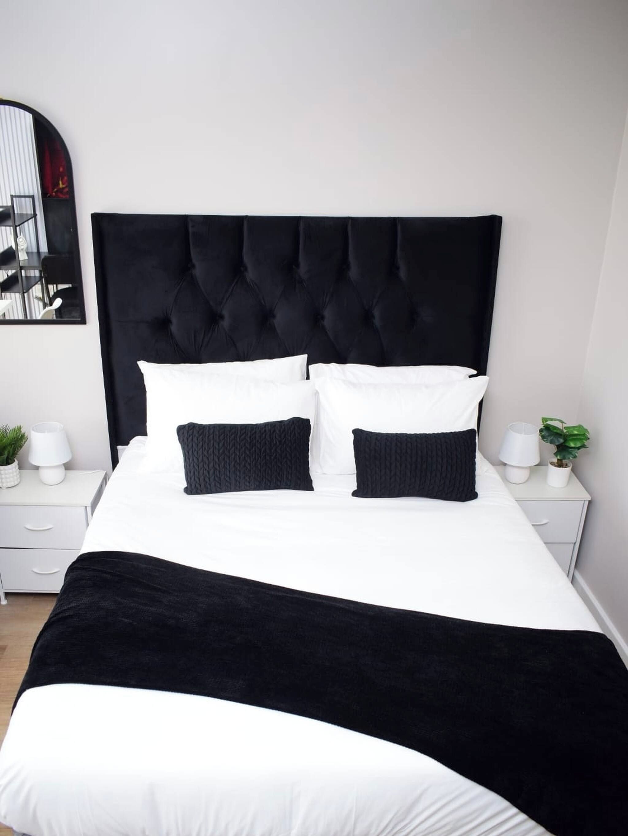 A bed with a tufted headboard, white bedding, and two black pillows.