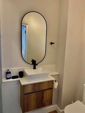 A bathroom with a white sink, a black faucet, a wooden cabinet, a mirror, and a toilet. - Saxon Square Voyage Work, Rest & Recharge (Johannesburg)