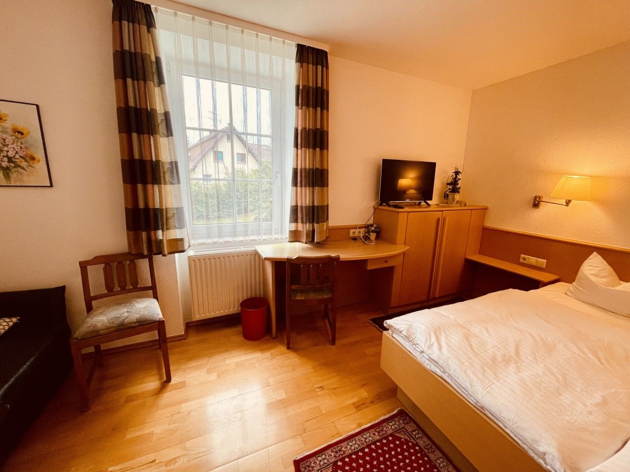 Ein Hotelzimmer mit Bett, Schreibtisch, Stuhl, Fernseher und einem Fenster mit Vorhängen.
