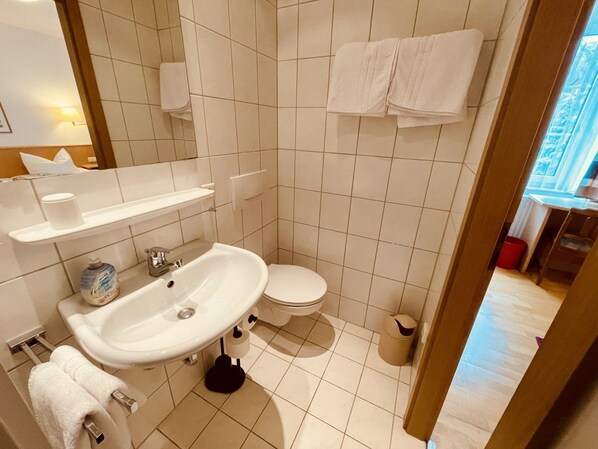 Une salle de bain avec un lavabo, des toilettes et un miroir. Des serviettes sont accrochées au mur et une poubelle est posée sur le sol.