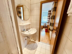 Et badeværelse med vask, spejl og bruseområde.