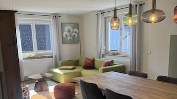 En moderne stue med et træspisebord, sorte stole, en grøn sofa og hængende lamper.