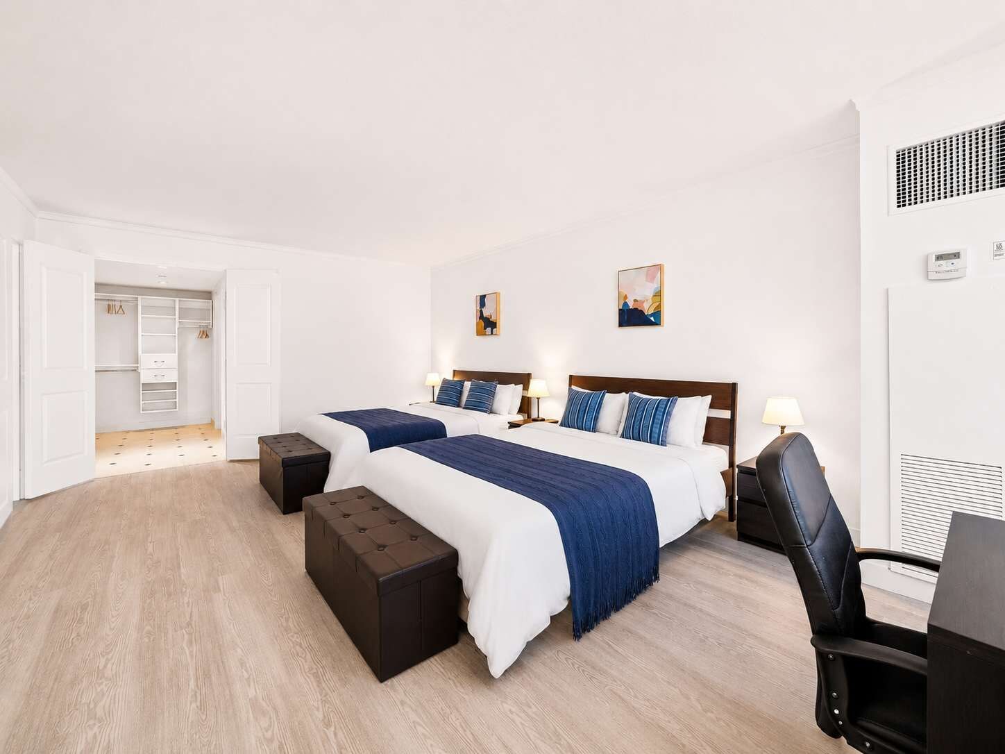 A hotel room with two beds, a desk, a chair, and a walk-in closet.