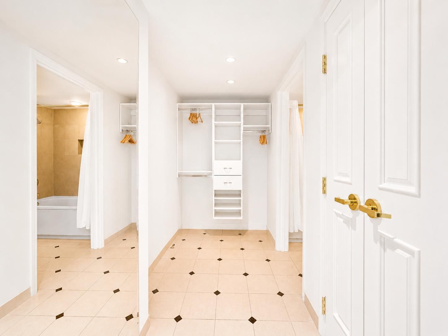 A hallway with a walk-in closet, a shower area, and a door with a gold handle.