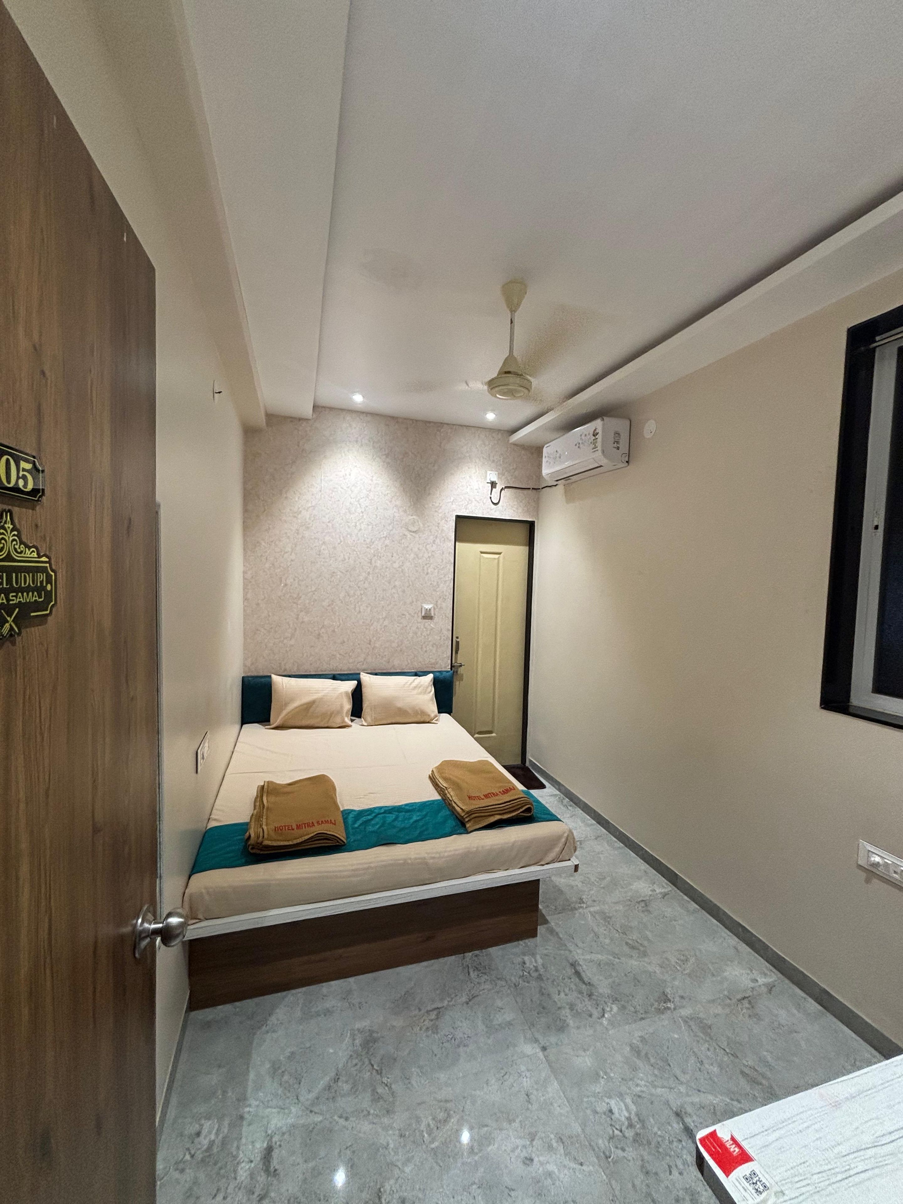 Una habitación de hotel con una cama, una puerta de madera, un ventilador de techo y una ventana.