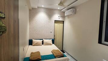 Una habitación de hotel con una cama, una puerta de madera, un ventilador de techo y una ventana.