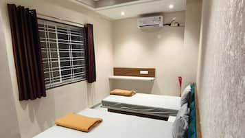 Una habitación de hotel con cama, aire acondicionado, ventana con cortinas y ventilador de techo.