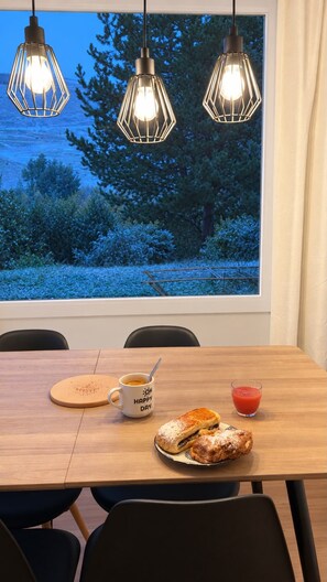Een eettafel met een koffiekop, een glas sap en een gebakje. Drie hanglampen hangen erboven.
