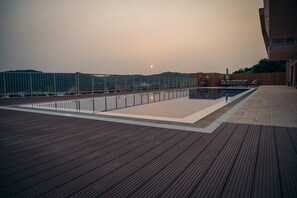 A rooftop pool area with a wooden deck, a metal fence, and a view of the sunset. - Stefanos Rock, Villa (Corfu)