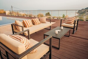 A poolside area with lounge chairs and a table, overlooking a body of water and a hilly landscape. - Stefanos Rock, Villa (Corfu)