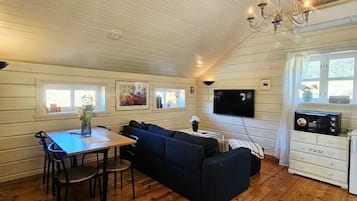 Een gezellige woonkamer met een houten plafond, een televisie, een bank, een eettafel met stoelen, en een keuken met een magnetron.