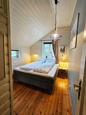 A bedroom with a sloped ceiling, a bed with floral bedding, a hanging light fixture, and a window with curtains. - New Listing (Vestland)