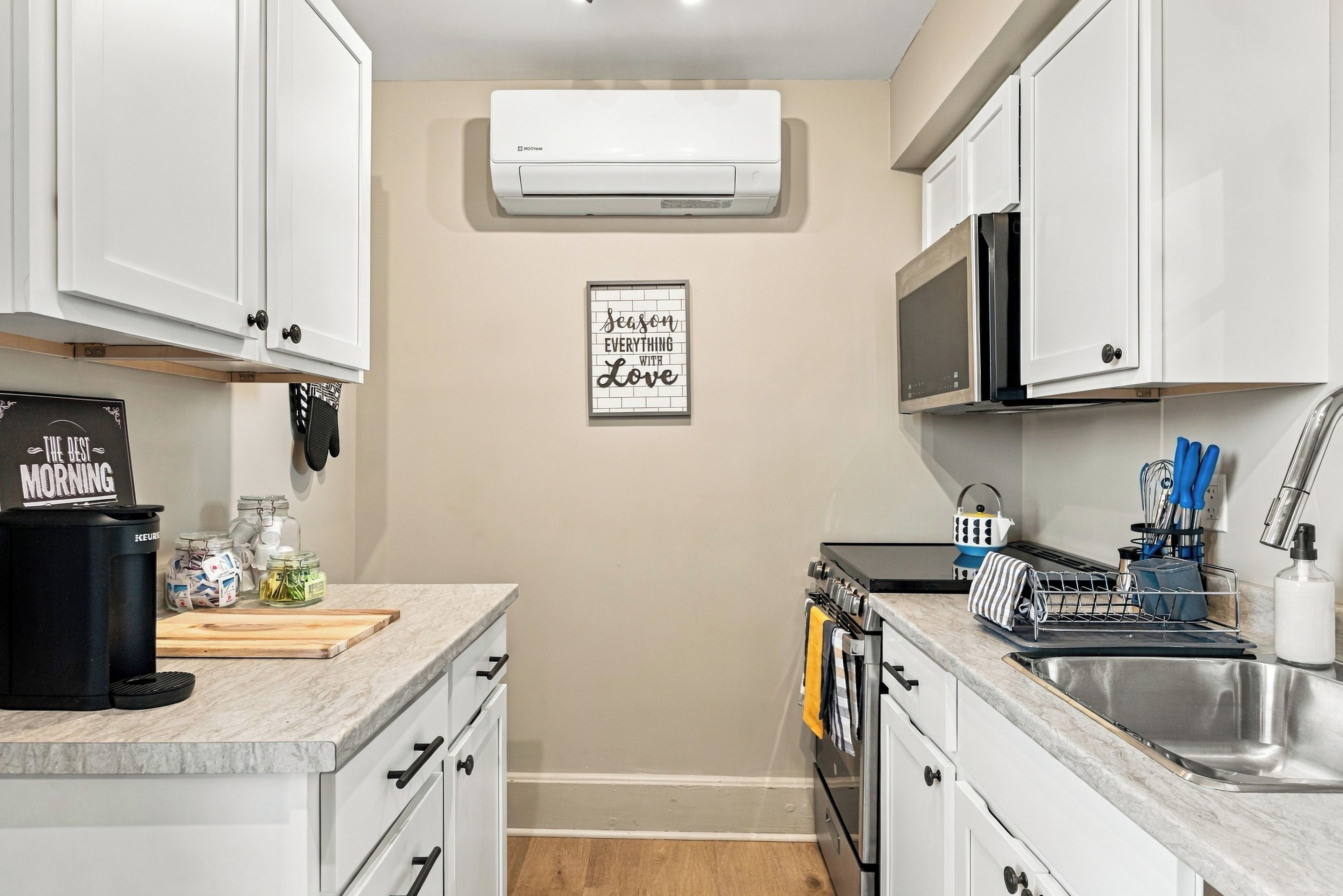 A modern kitchen with white cabinets, a microwave, an oven, and a coffee machine.