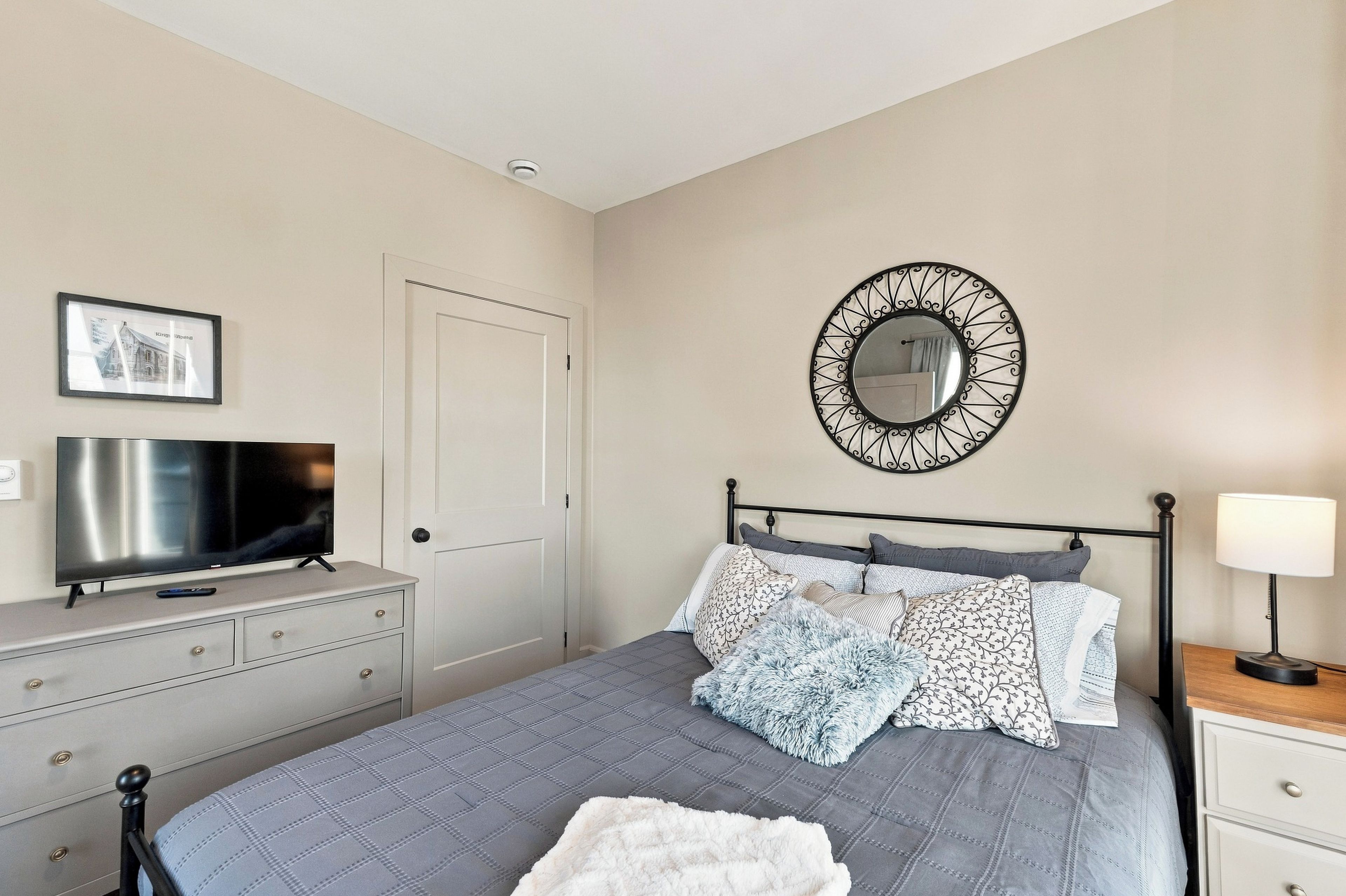 A bedroom with a bed, a television, a dresser, a mirror, and a bedside lamp.