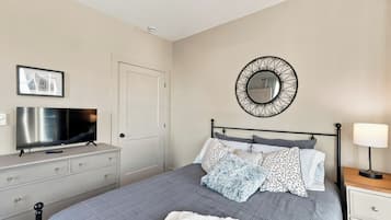 A bedroom with a bed, a television, a dresser, a mirror, and a bedside lamp.