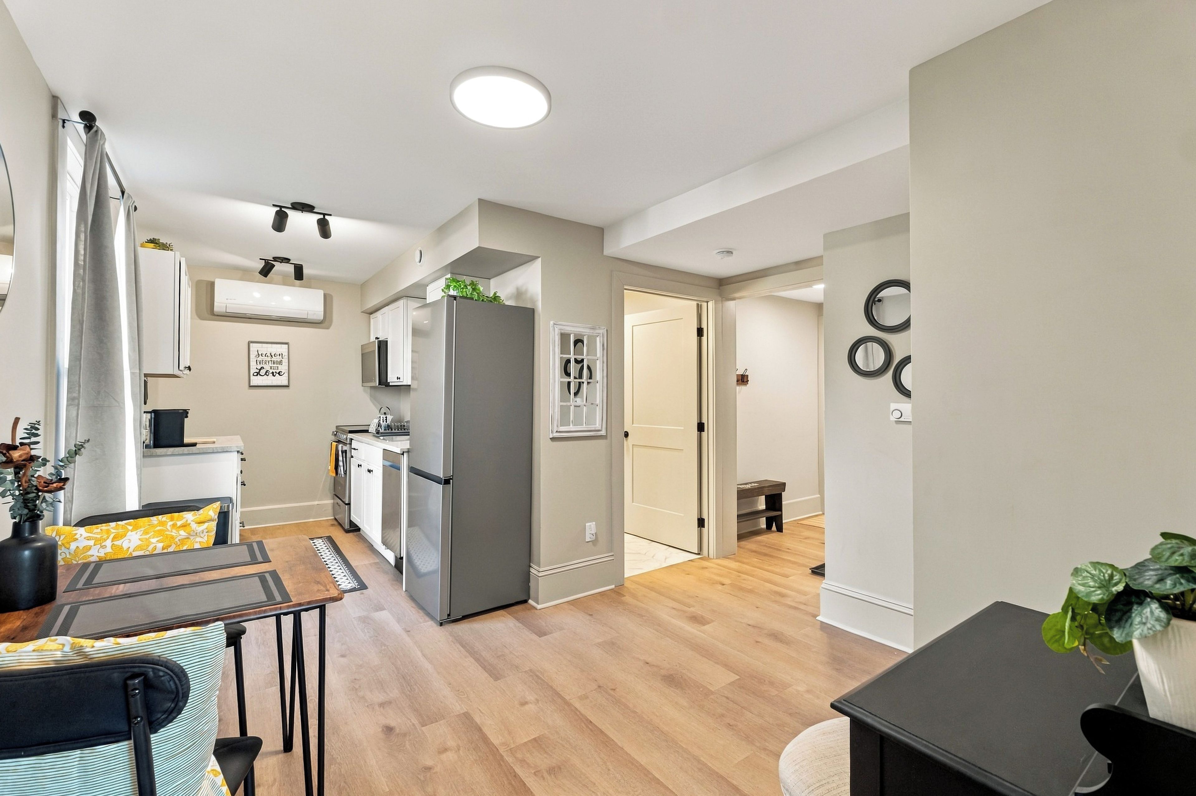 A modern kitchen with a refrigerator, oven, and microwave. There is a dining area with a table and chairs. The room has wooden flooring and white walls.