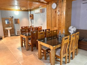 Un comedor con una mesa y sillas de madera, un reloj en la pared y un ventilador en el suelo.