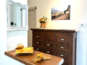 Una habitación con un aparador de madera, un espejo, un florero con flores y un cuadro en la pared.