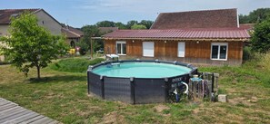 A residential backyard with a circular above-ground pool, a wooden deck, and a house with a red roof.
