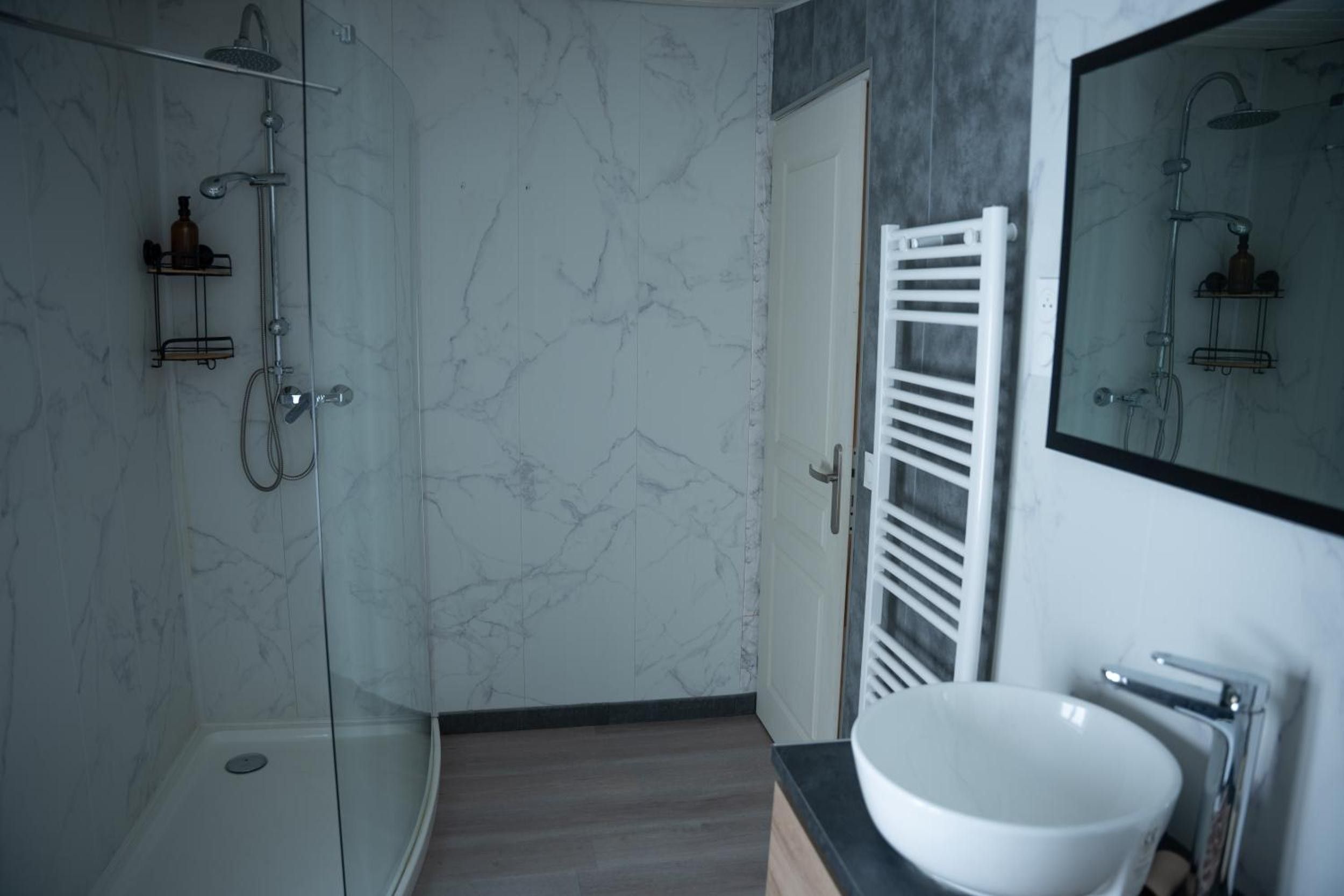 A modern bathroom with a glass shower enclosure, a white sink, and a marble wall.
