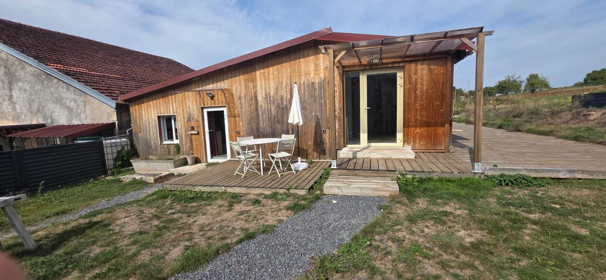 A wooden house with a patio, a door, and a small table with chairs.