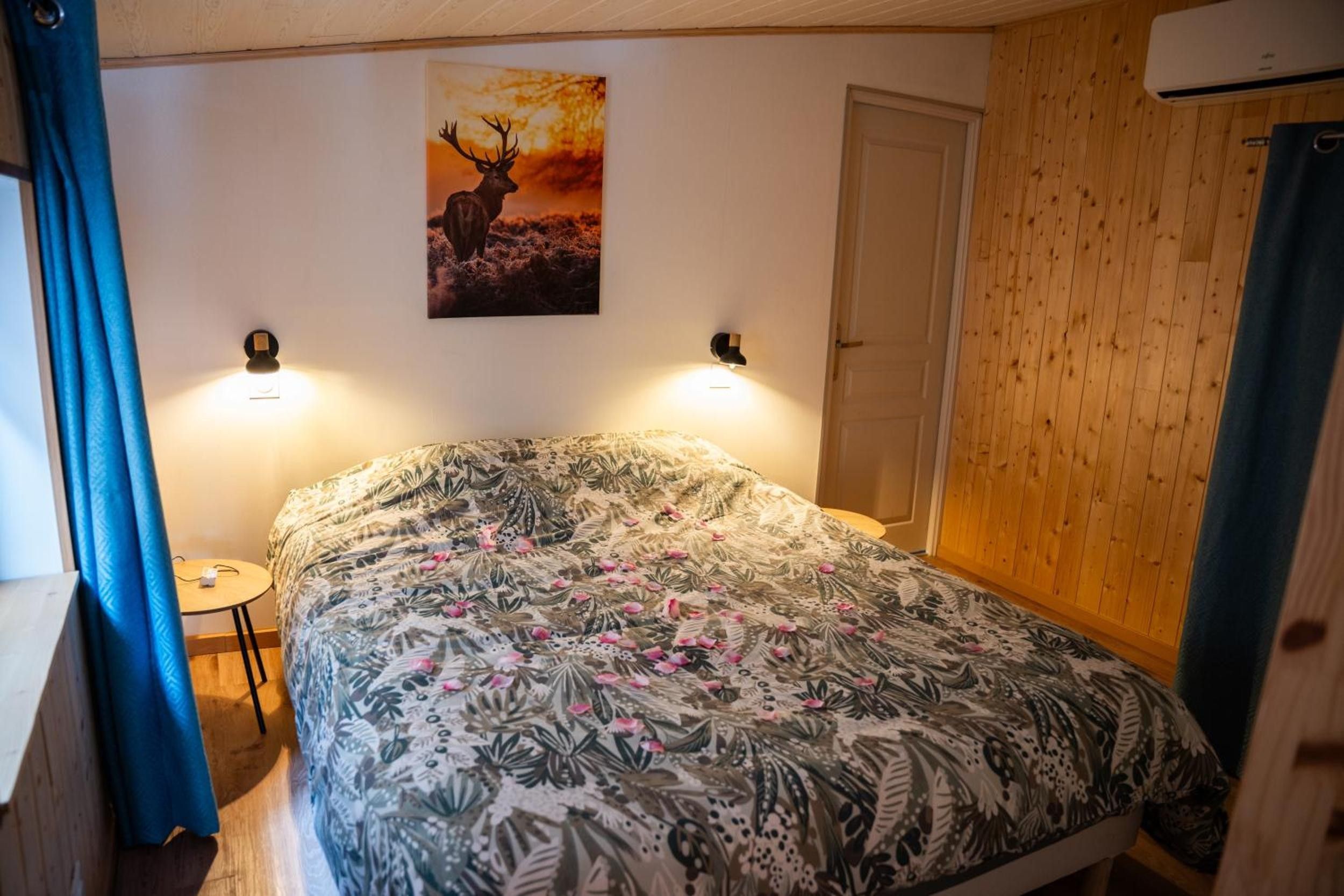 Une chambre à coucher comprenant un lit, un tableau accroché au mur, deux appliques murales, une porte et une petite table.