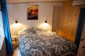 A bedroom with a bed, a wall-mounted picture, two wall sconces, a door, and a small table.