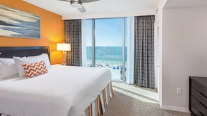 A hotel room with a bed, a ceiling fan, a view of the beach, and a large window. - Soak Up the Sunshine at Wyndham Clearwater Beach-1 Bedroom Deluxe (Clearwater)