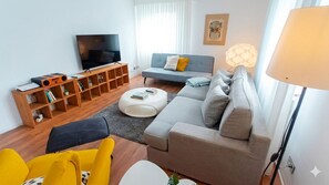 A modern living room with a flat-screen TV, a grey sofa, a yellow armchair, and a wooden bookshelf. - New Listing (Wendelstein)