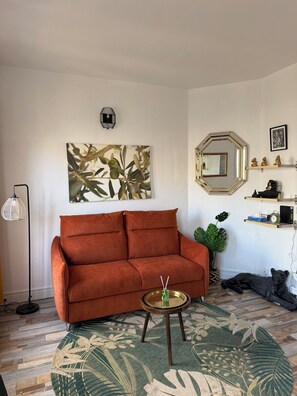 A living room with a sofa, a round coffee table, a large wall art piece, a mirror, and a plant. - New Listing (Vanves)
